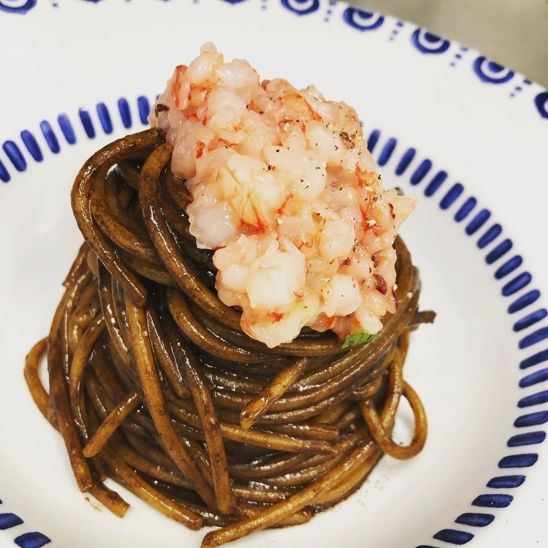 Teller mit Tagliolini mit schwarzem Knoblauch und Meeresfrüchten